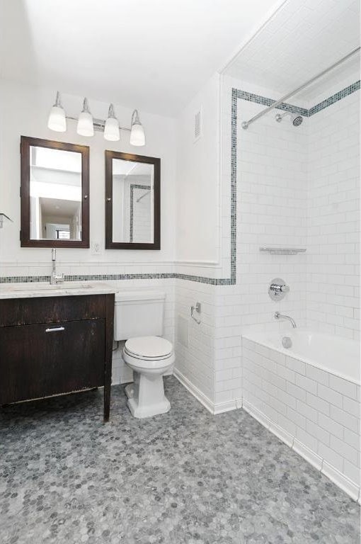 full bathroom with vanity, tiled shower / bath, tile walls, and toilet