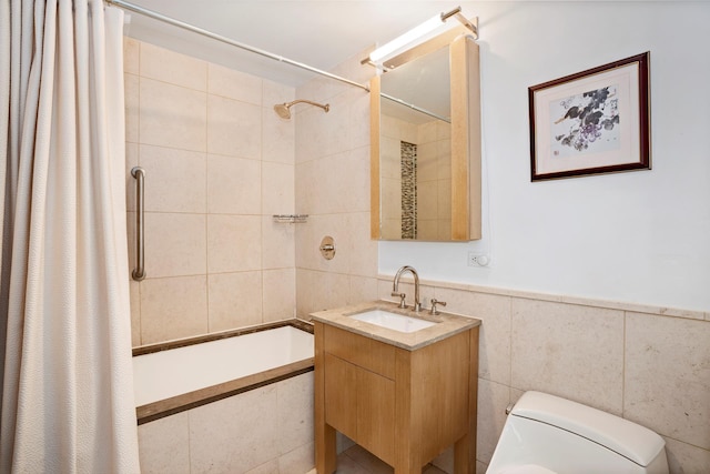 full bath with toilet, a wainscoted wall, tiled shower / bath, vanity, and tile walls