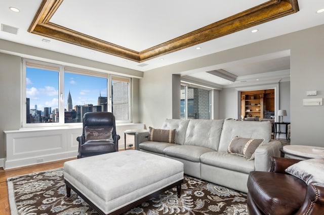 living room featuring wood finished floors, visible vents, crown molding, a city view, and a raised ceiling