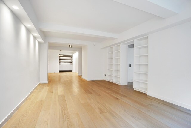 spare room featuring beam ceiling and light hardwood / wood-style flooring