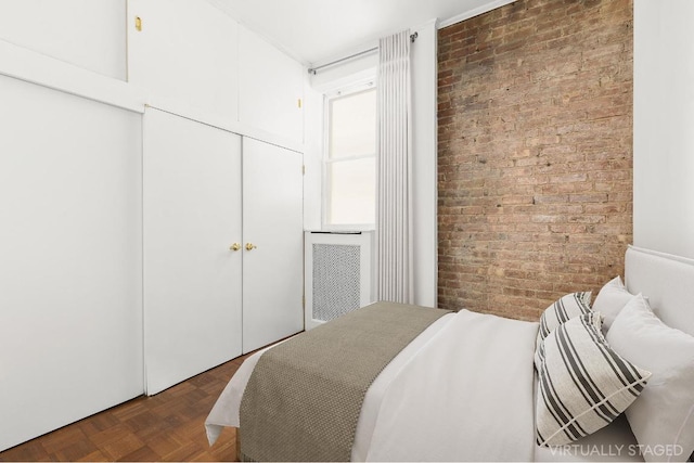 bedroom with parquet flooring, a closet, and brick wall