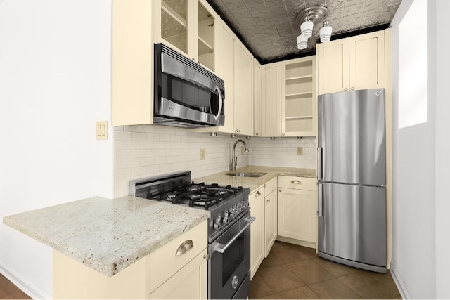 kitchen with tasteful backsplash, sink, dark tile patterned floors, stainless steel appliances, and light stone countertops