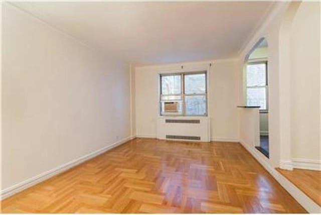 empty room with ornamental molding, parquet flooring, and radiator