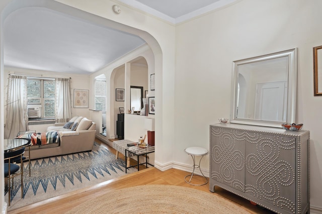 living area featuring wood finished floors, baseboards, arched walkways, and ornamental molding