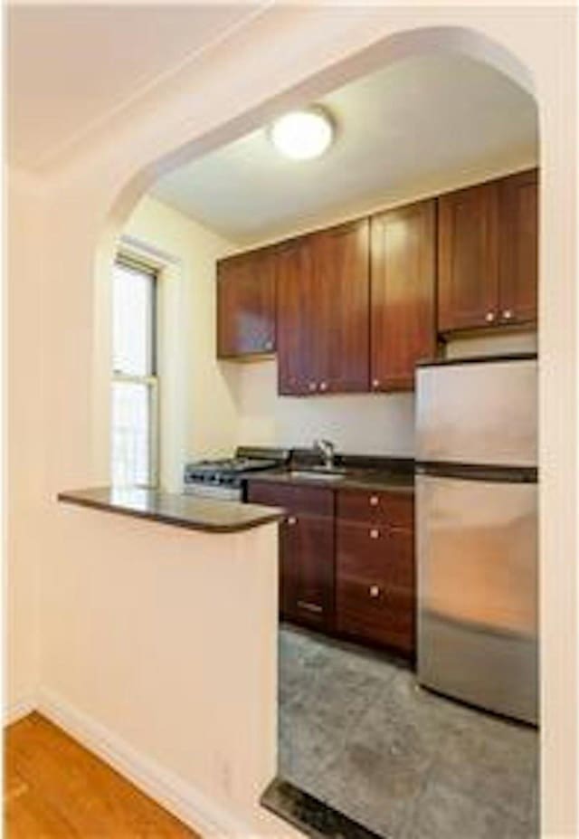 kitchen with a peninsula, arched walkways, freestanding refrigerator, a sink, and dark countertops