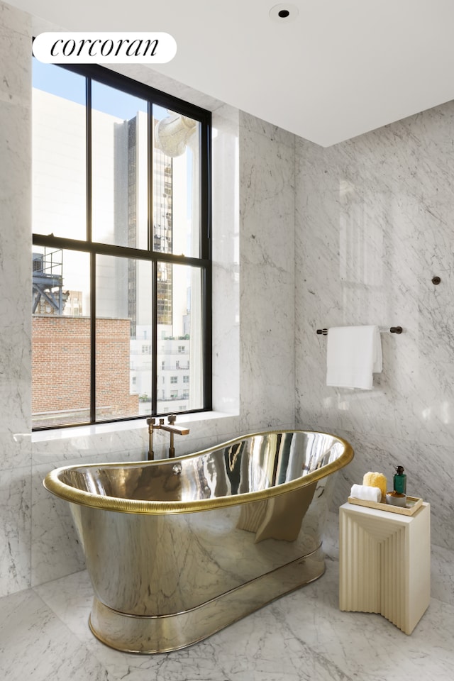 full bath with marble finish floor, stone wall, and a freestanding bath