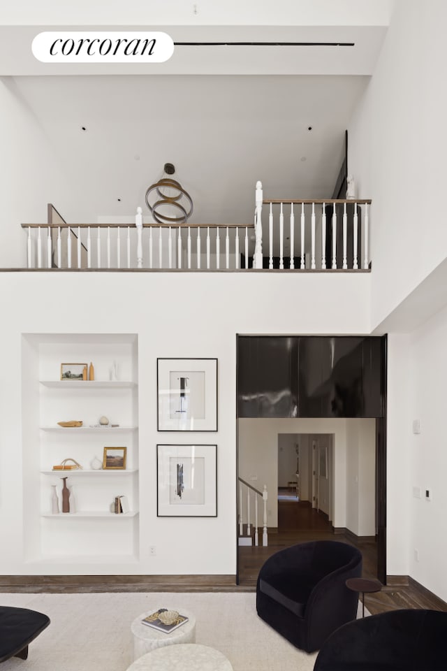 living area with built in features, stairway, a towering ceiling, and wood finished floors