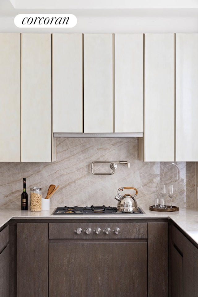 kitchen featuring white cabinets, light countertops, dark brown cabinets, tasteful backsplash, and stainless steel gas stovetop