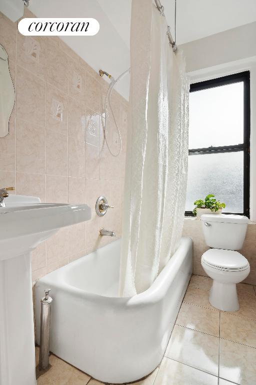 bathroom with tile patterned flooring, shower / bath combo, tile walls, and toilet