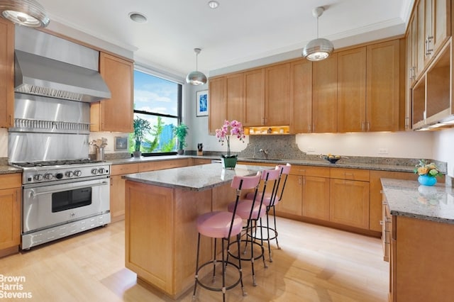 kitchen with a kitchen island, decorative light fixtures, high end range, light stone counters, and wall chimney exhaust hood