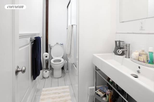 full bathroom with combined bath / shower with glass door, sink, tile walls, toilet, and tile patterned floors