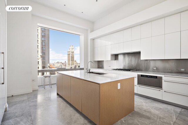 kitchen featuring sink, tasteful backsplash, an island with sink, white cabinets, and stainless steel gas stovetop