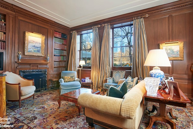 sitting room featuring built in shelves, wooden walls, ornamental molding, and a premium fireplace