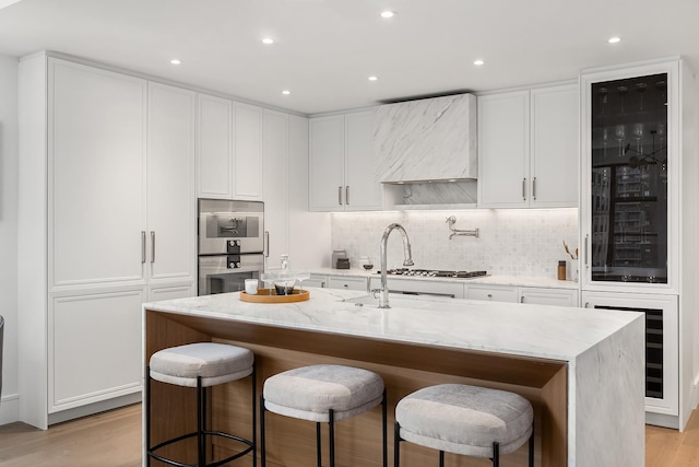 kitchen with light stone countertops, decorative backsplash, a kitchen bar, light wood-style flooring, and white cabinetry