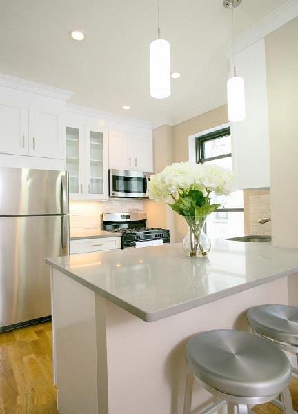 kitchen featuring light hardwood / wood-style floors, appliances with stainless steel finishes, white cabinets, crown molding, and a kitchen bar