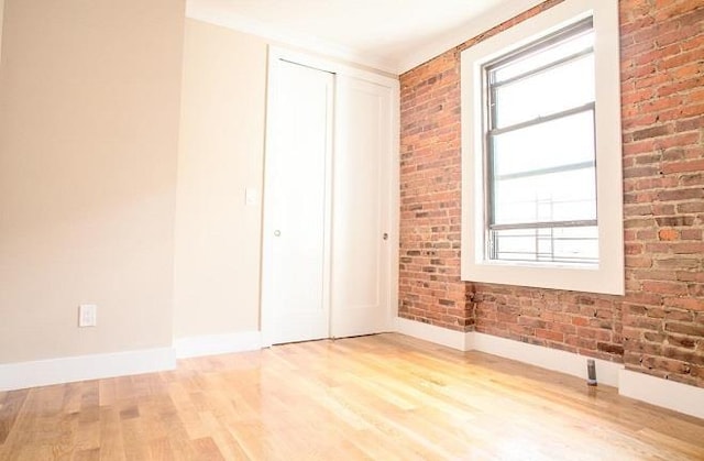 unfurnished room with a wealth of natural light, baseboards, brick wall, and light wood finished floors