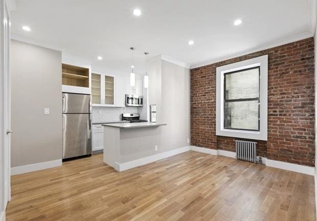 kitchen with white cabinetry, hanging light fixtures, brick wall, and stainless steel appliances