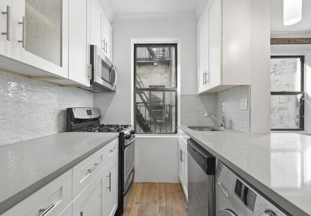 kitchen with appliances with stainless steel finishes, sink, white cabinetry, and ornamental molding