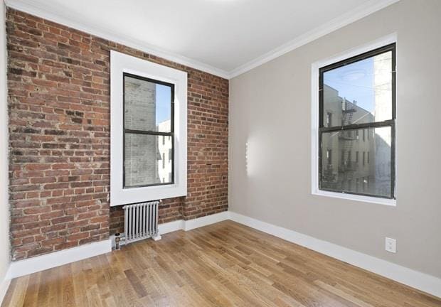 unfurnished room featuring radiator, brick wall, crown molding, and light hardwood / wood-style floors