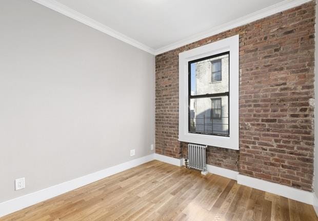 spare room with radiator, brick wall, ornamental molding, and hardwood / wood-style floors