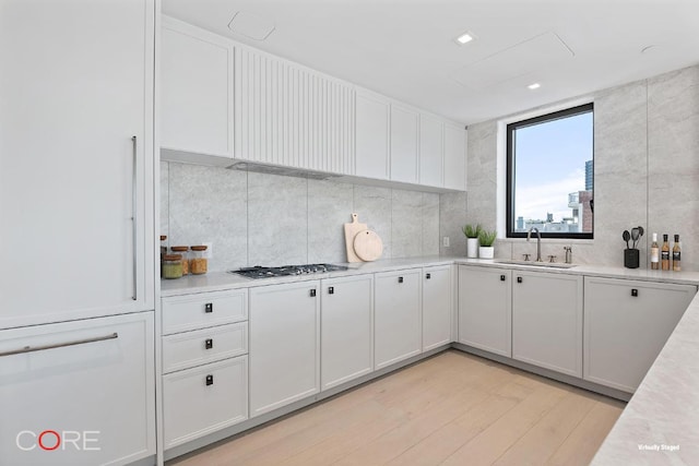 kitchen with stainless steel gas stovetop, white cabinetry, sink, decorative backsplash, and light hardwood / wood-style floors