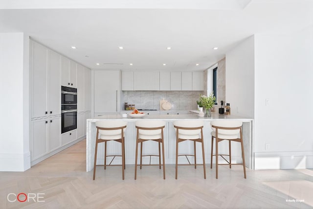 kitchen with a kitchen bar, white cabinetry, kitchen peninsula, double oven, and backsplash