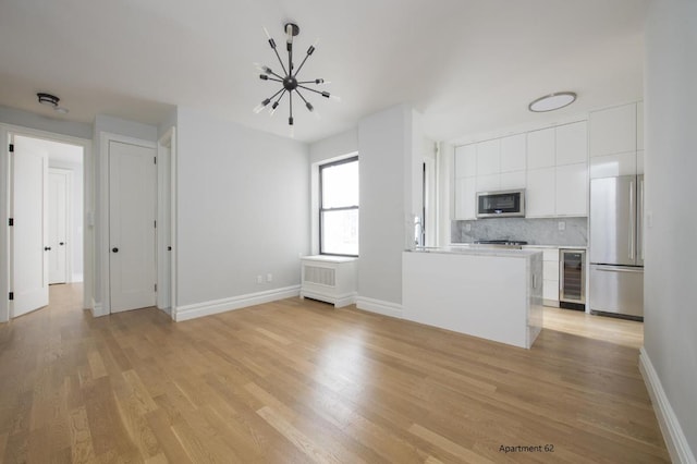 kitchen with light hardwood / wood-style flooring, appliances with stainless steel finishes, beverage cooler, decorative backsplash, and white cabinets