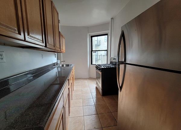 kitchen with light tile patterned floors, dark stone counters, sink, and stainless steel appliances