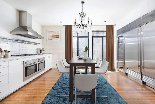 kitchen featuring exhaust hood, pendant lighting, stainless steel appliances, light hardwood / wood-style floors, and white cabinets