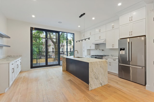 kitchen with white cabinets, light stone counters, light hardwood / wood-style floors, high end fridge, and a center island with sink