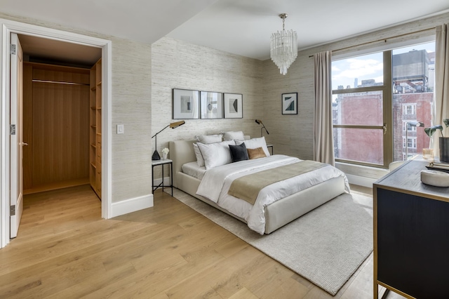 bedroom with light wood-type flooring, a walk in closet, wallpapered walls, baseboards, and a chandelier