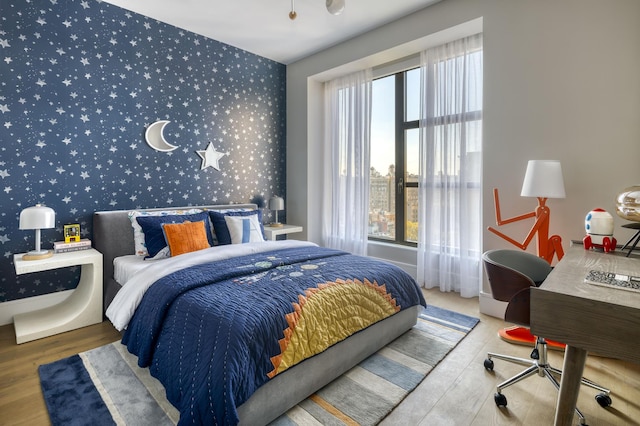 bedroom with wood finished floors, an accent wall, and wallpapered walls