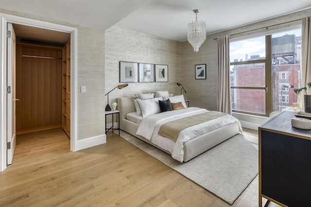 bedroom featuring baseboards, wallpapered walls, an inviting chandelier, a spacious closet, and light wood-style floors