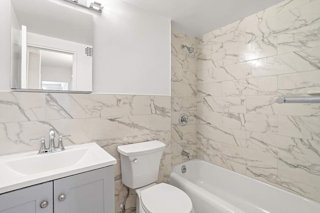 full bathroom featuring tiled shower / bath, vanity, toilet, and tile walls