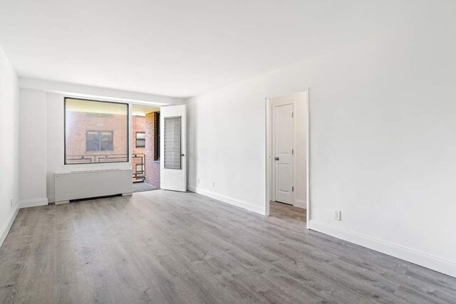 empty room with hardwood / wood-style flooring and radiator heating unit