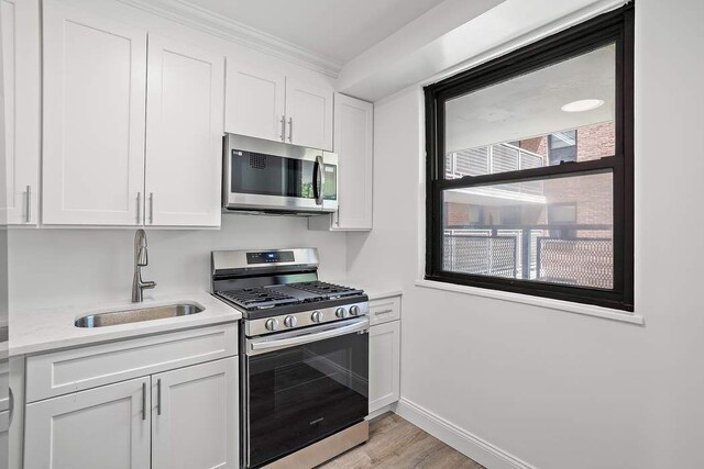 kitchen with appliances with stainless steel finishes, light stone countertops, sink, and white cabinets