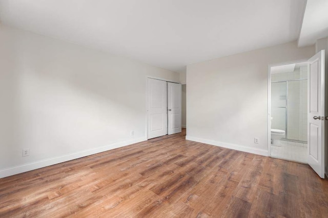 unfurnished bedroom featuring hardwood / wood-style flooring, ensuite bath, and a closet