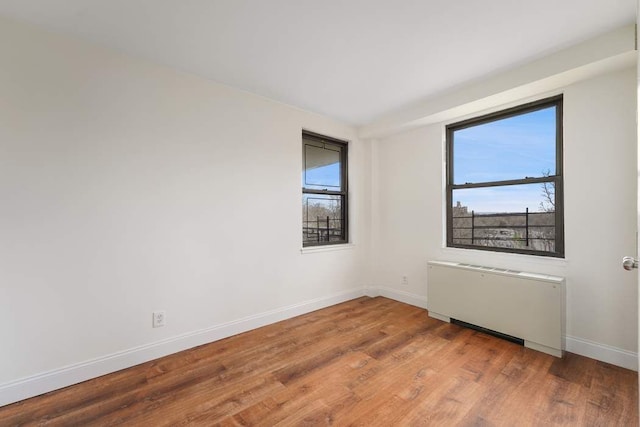 spare room featuring hardwood / wood-style flooring, a healthy amount of sunlight, and radiator heating unit