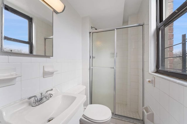 bathroom with a shower with door, sink, tile walls, and toilet