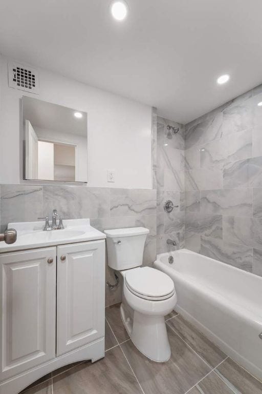 full bathroom with tile walls, vanity, toilet, and tiled shower / bath