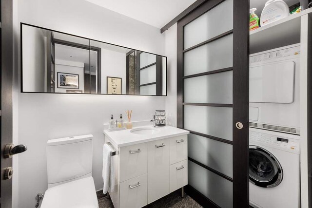 bathroom with stacked washer / dryer, vanity, and toilet