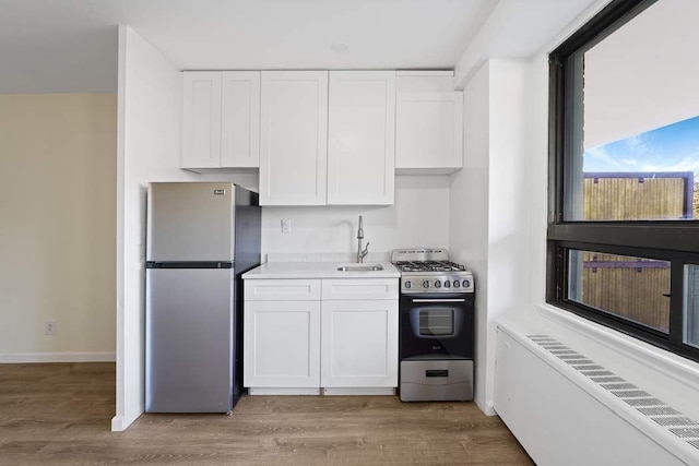 kitchen featuring appliances with stainless steel finishes, radiator heating unit, white cabinetry, sink, and light hardwood / wood-style flooring