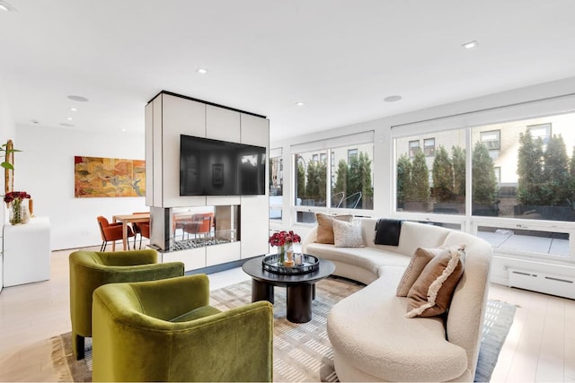 living room with baseboard heating, a multi sided fireplace, and light wood-type flooring