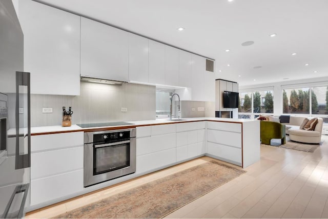 kitchen with black electric cooktop, oven, sink, and white cabinets