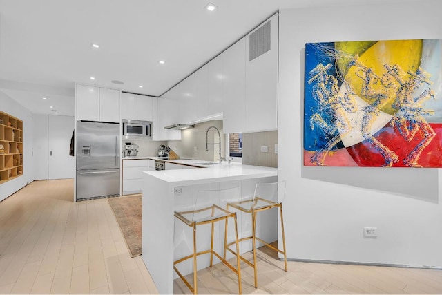 kitchen featuring white cabinetry, sink, a breakfast bar area, built in appliances, and kitchen peninsula