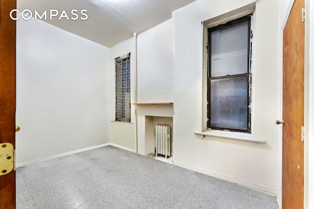 empty room with radiator heating unit, baseboards, and tile patterned floors