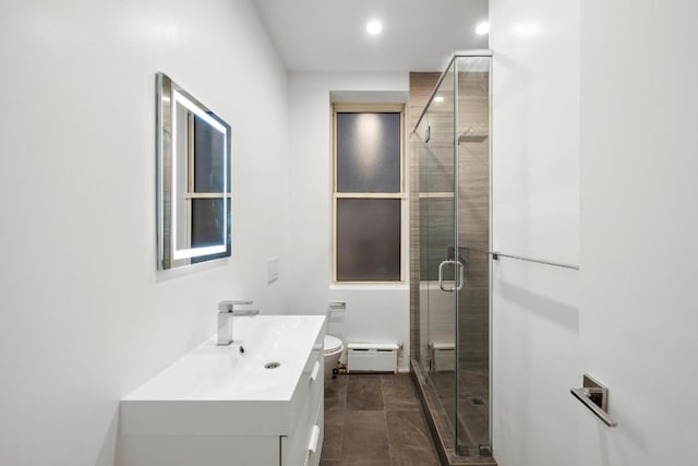 bathroom with toilet, baseboard heating, a shower with shower door, and vanity