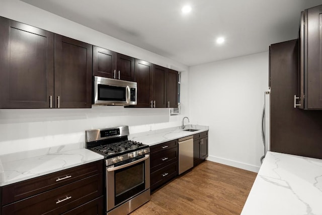 kitchen with appliances with stainless steel finishes, sink, light stone counters, dark brown cabinets, and light hardwood / wood-style flooring