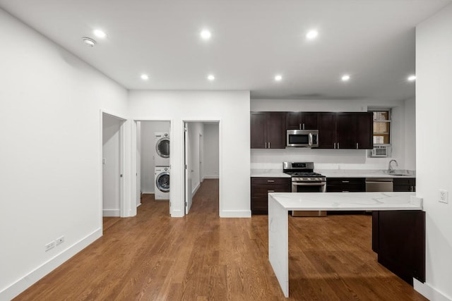 kitchen featuring stacked washer / drying machine, sink, dark brown cabinetry, light wood-type flooring, and appliances with stainless steel finishes