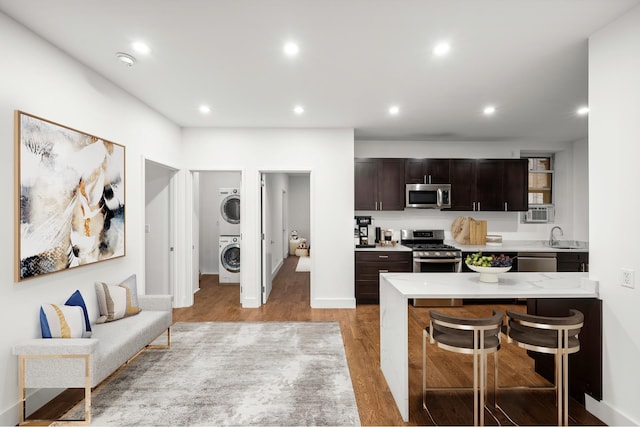 57 W 58th St Unit 6Ab, New York City, NY 10019 - kitchen with stainless steel appliances, stacked washer and clothes dryer, light wood finished floors, recessed lighting, and dark brown cabinetry